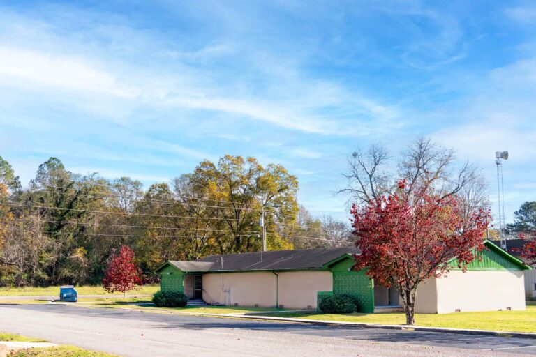 A picturesque view of the New Market Clinic in the fall, framed by vibrant green and crimson foliage. The clinic stands peacefully amidst the colorful trees under a clear blue sky.