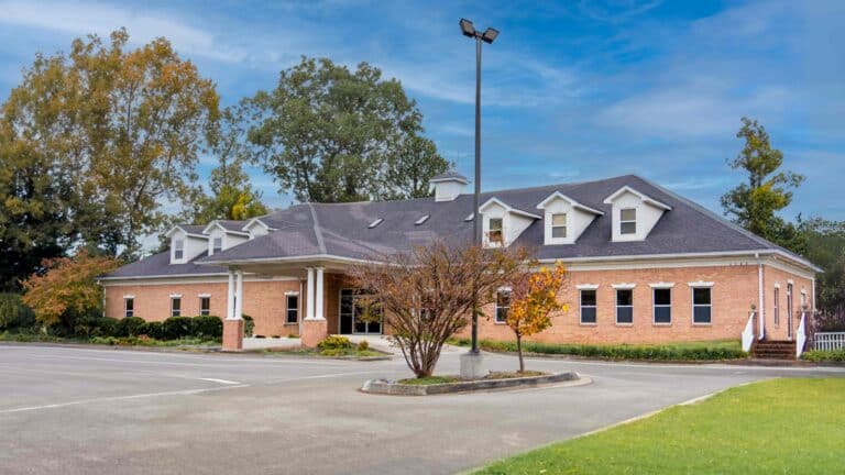 Front view of Toney Family Health Center building featuring an awning at the entrance, set against a backdrop of clear blue skies and surrounded by lush greenery.